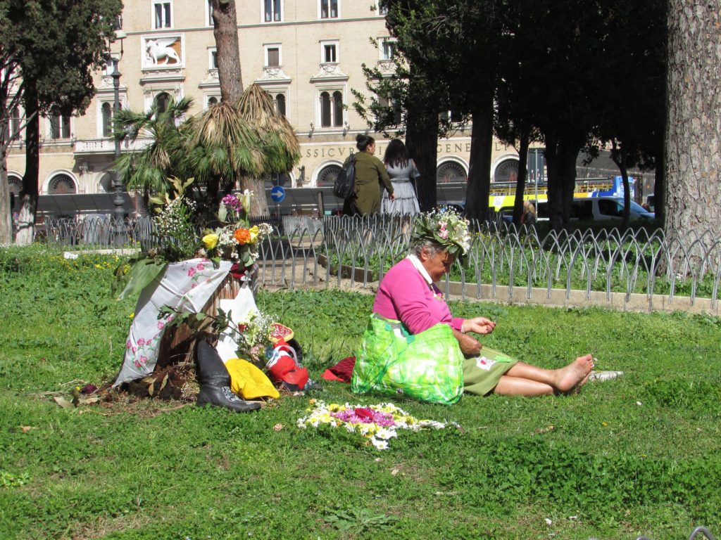 Olda lady in colourful otfit sits on the grass in the cits of Rome, Italy