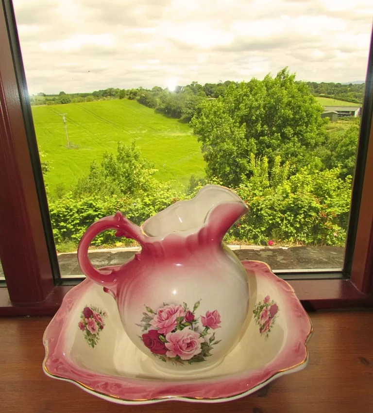 old decorative pink jar on the plate, on the windowsill overlooking very green meadow in Ireland