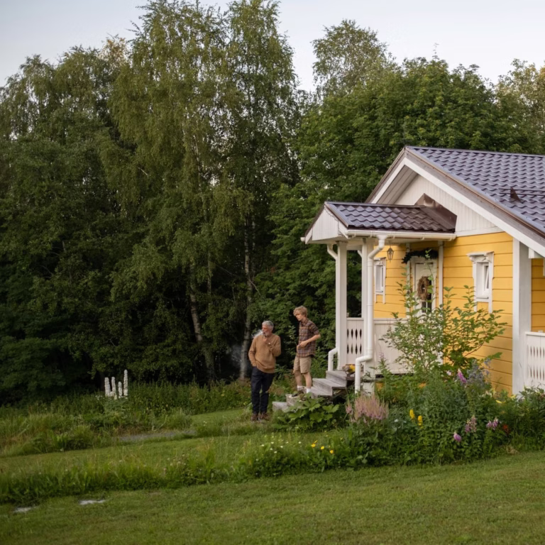 yellow woden house in green yard and two people infront